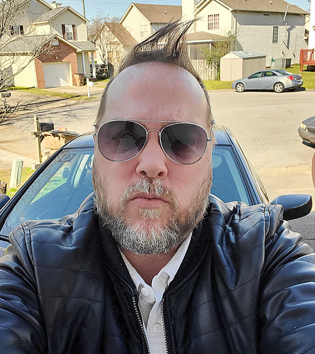 Kene Bell wearing aviator sunglasses and a leather jacket outdoors