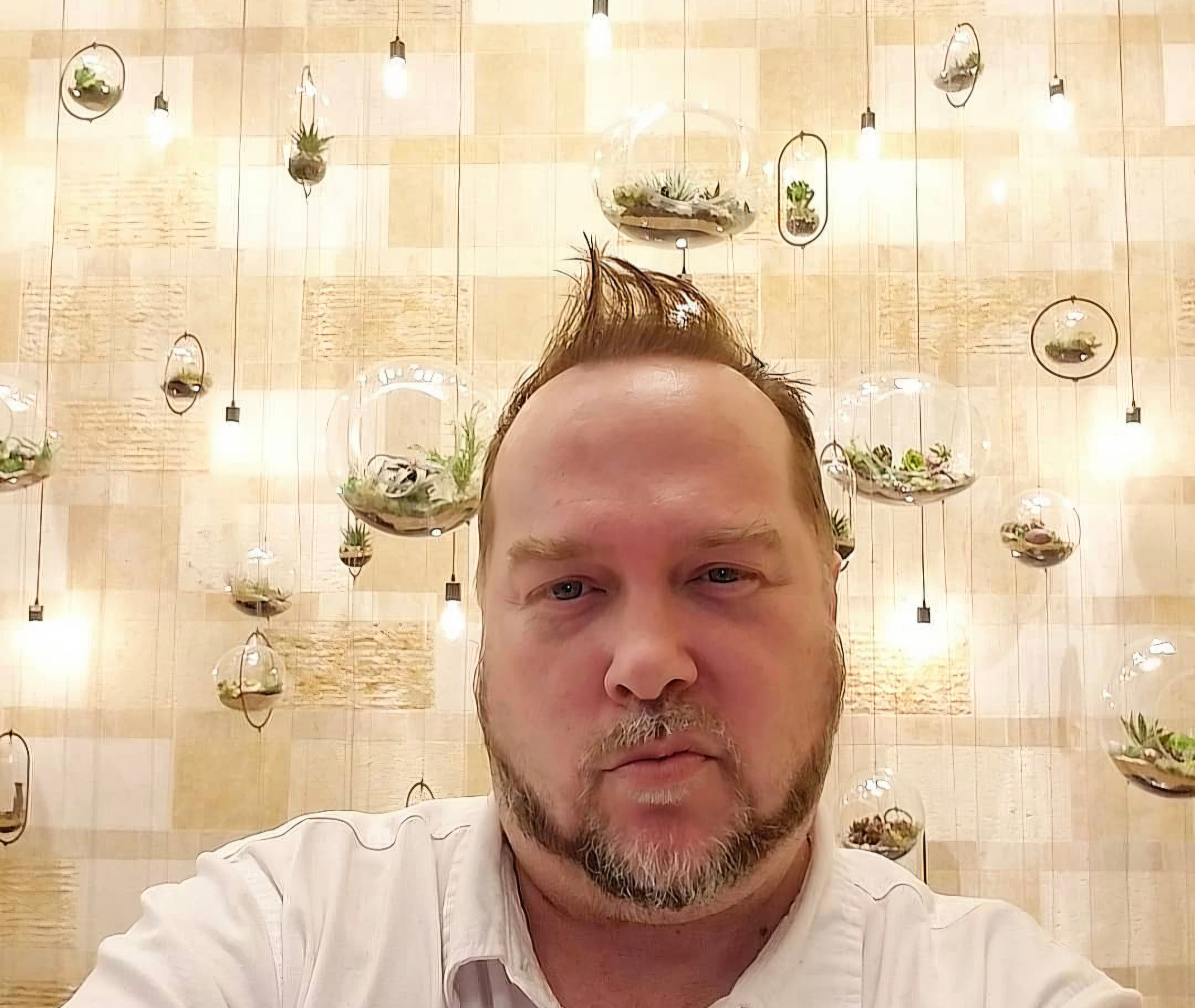 Kene Bell photographed in front of a wall of hanging glass terrariums