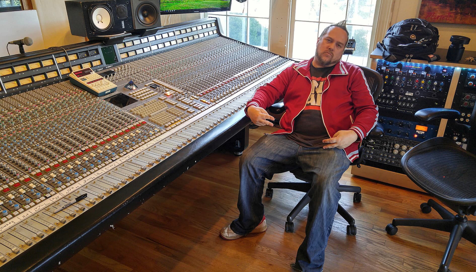 Kene Bell seated beside a large-format studio mixing console