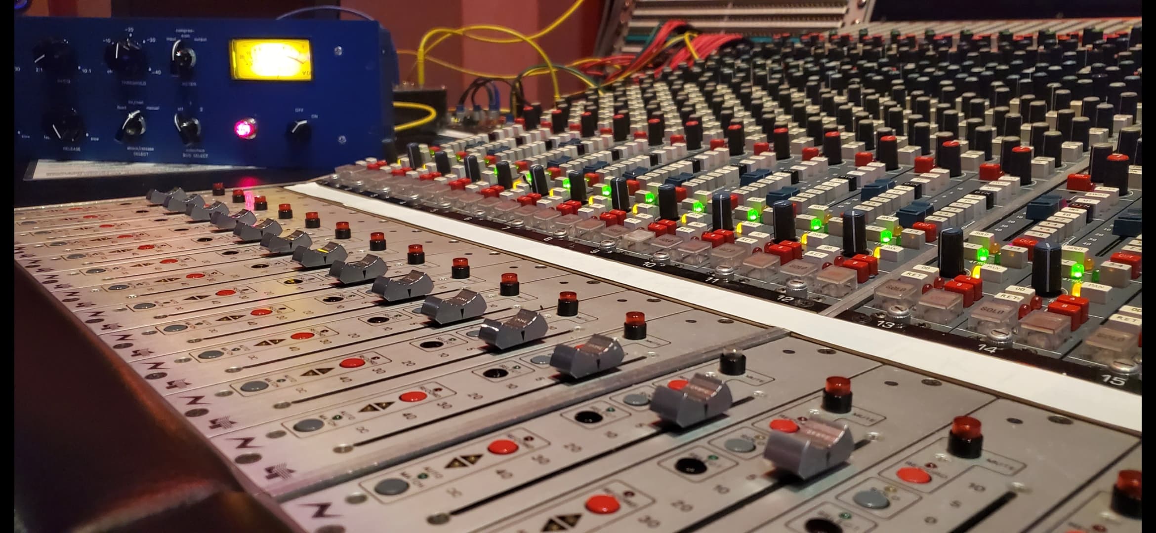 Close detail of an analog mixing console beside illuminated outboard equipment