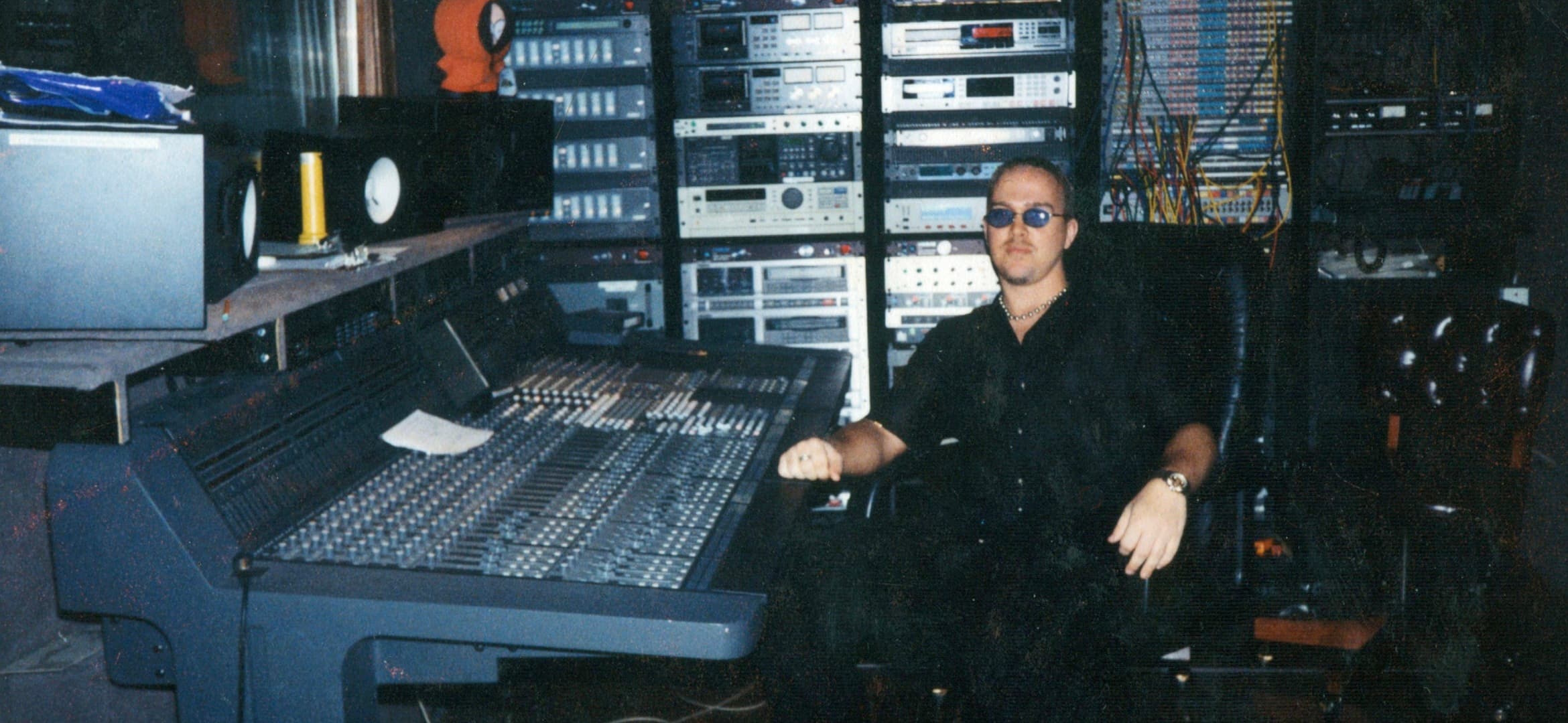 Earlier-era professional control room with a large console, extensive rack equipment, and a seated producer