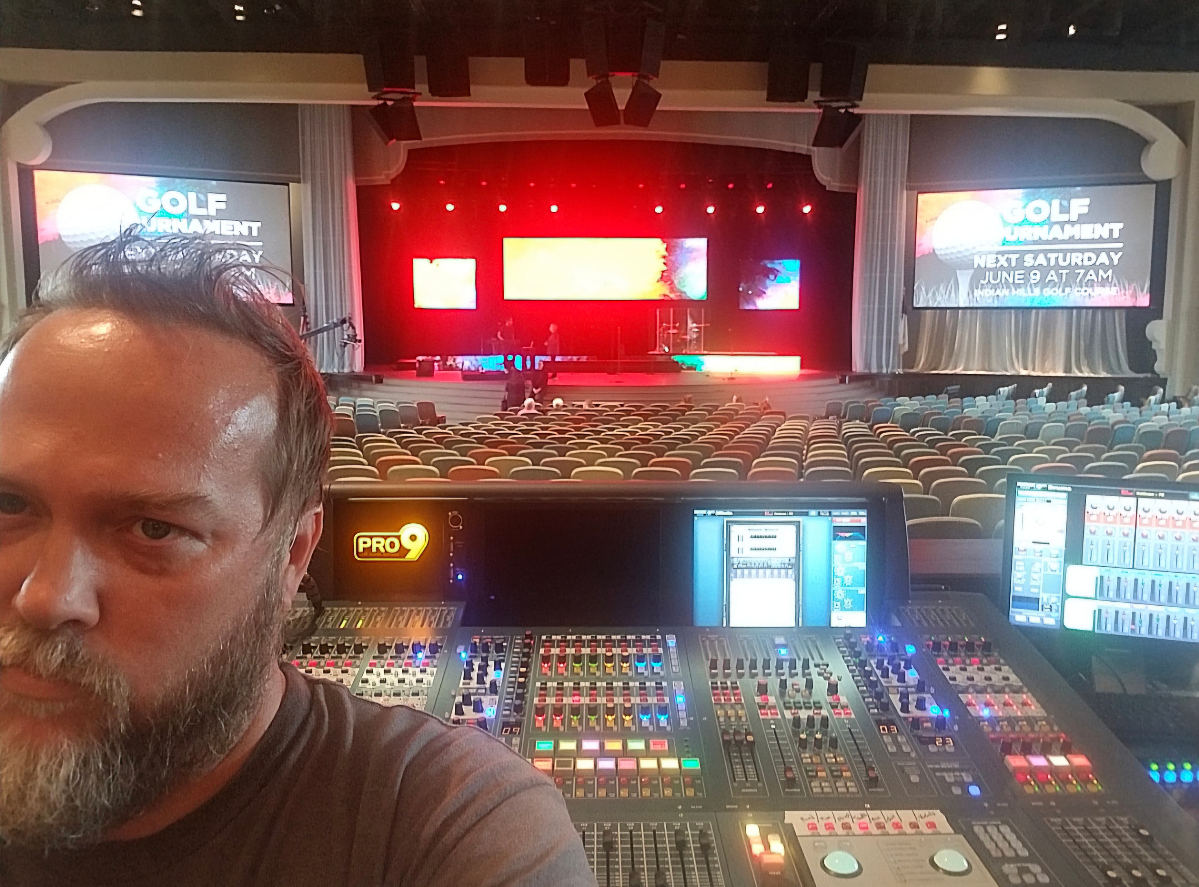 Kene Bell at a PRO9 live-sound console with an auditorium and stage behind him