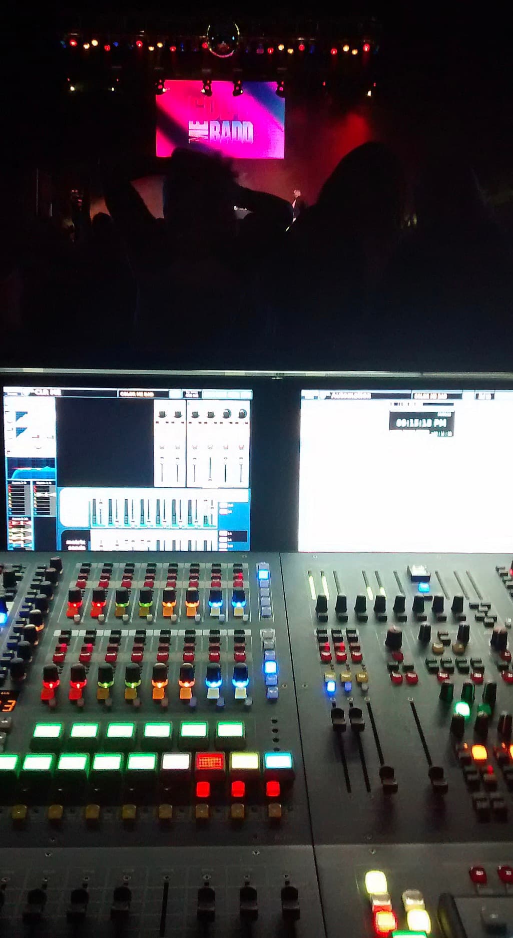 Live-sound console facing audience silhouettes and an illuminated performance stage